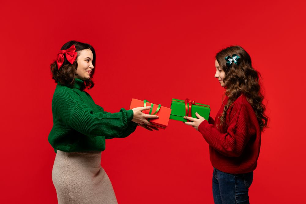 Mum and teenage daughter exchange holiday presents in red studio