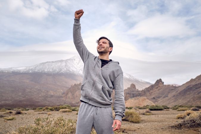 Delighted young man raising arm in success in mountainous area