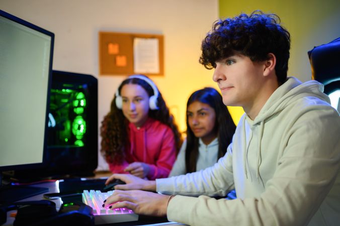 Concentrated young man sitting at table and playing on computer with multiracial teenage friends