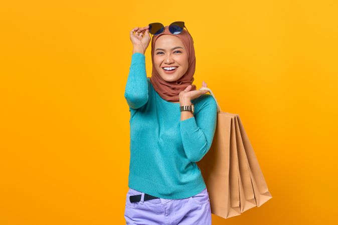 Happy Muslim woman adjusting her sunglasses with shopping bags on her back