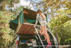 Woman standing in ladder opening tent over car 48B2RK