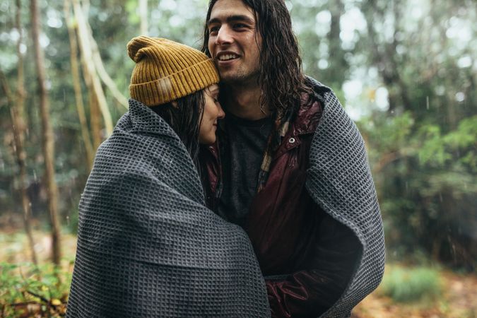 Couple wrapped in blanket under the rain outdoors
