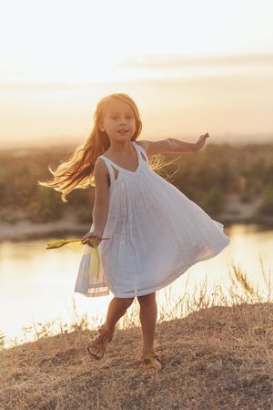 Blonde female child in dress playing in front of lake with star wand