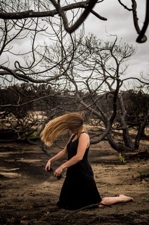 Woman posing on ground near dry trees