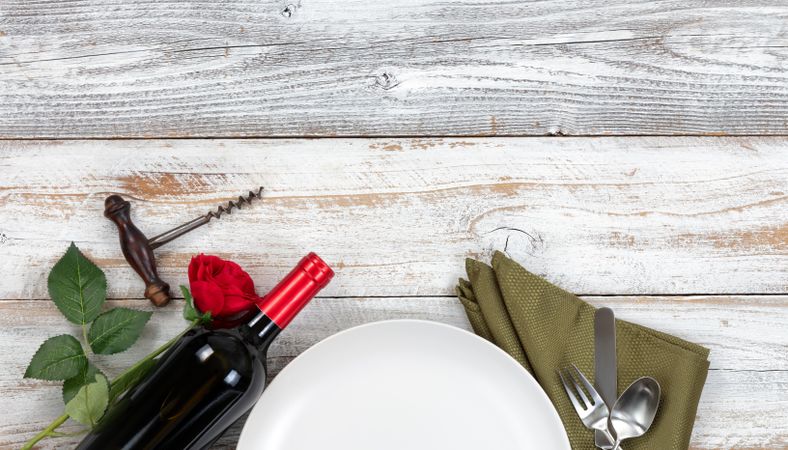 Top view of romantic dinner plate setting with red wine and rose on rustic table