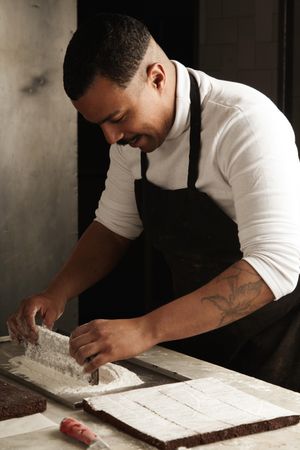 Black male chef working with powdered sugar to top chocolate slices with