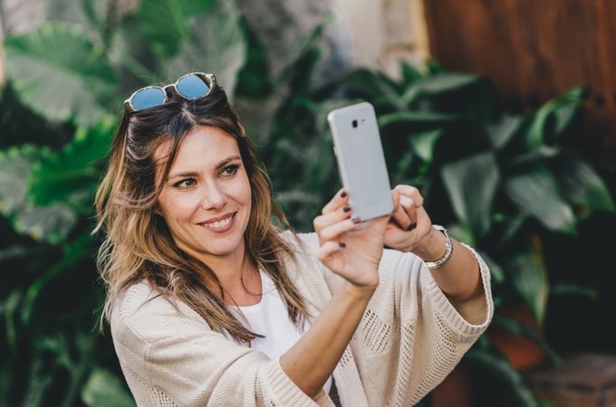 Smiling woman taking selfie in street city full of plants