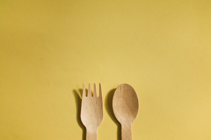 Top of disposable fork & spoon on yellow background with copy space