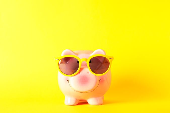 Happy piggy bank with sunglasses on yellow background, space for text. Finance, saving money