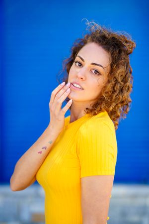 Woman with heart tattoos on arm touching face in front of blue background