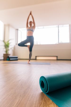 Yoga mat in fitness center with woman meditating at back