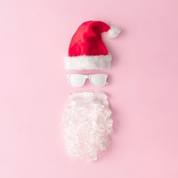 Santa face made of sunglasses, hat and beard on pink background
