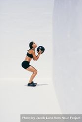 Female athlete squatting while holding a medicine ball 5aolAb
