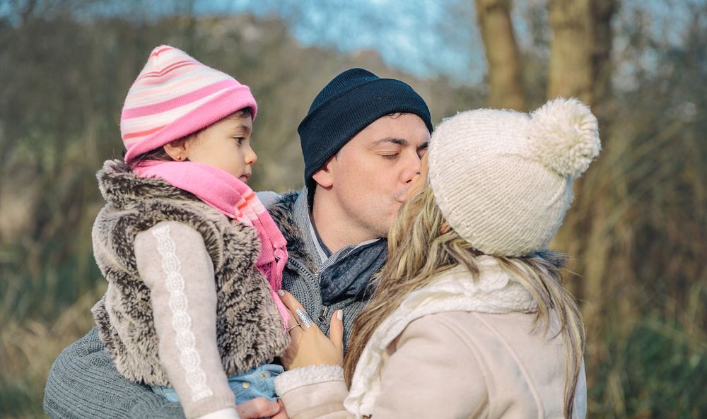 Mother and father kissing with daughter in arms