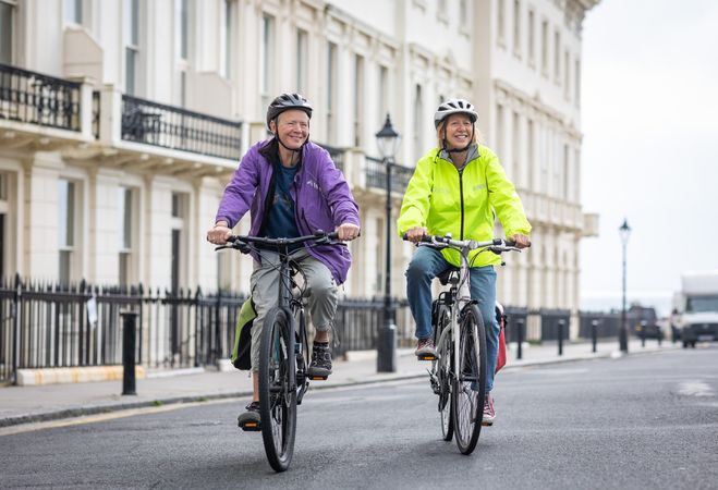 Two happy older people riding bikes through town