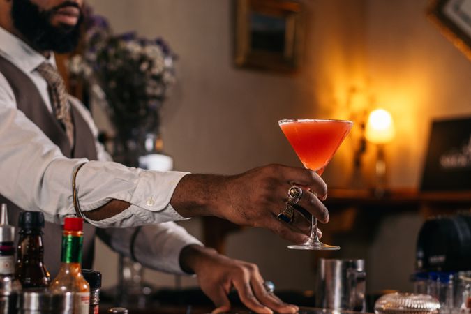 Cutout of a Black bartender offering a cocktail served in a martini glass in a traditional cocktail bar