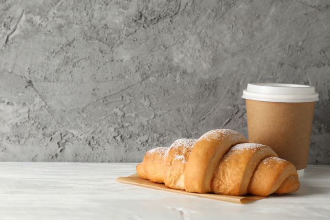 Croissant and paper cup on marble background, copy space