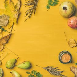 Autumn harvest fruit, leaves, and espresso on mustard yellow background