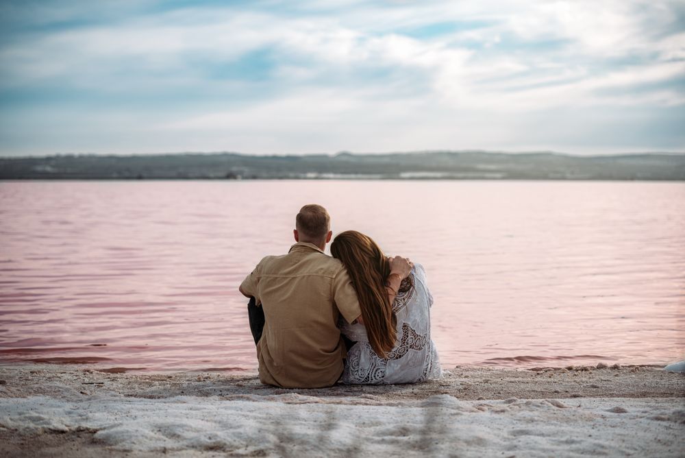 adorable couple sitting on an amazing beach with pink water