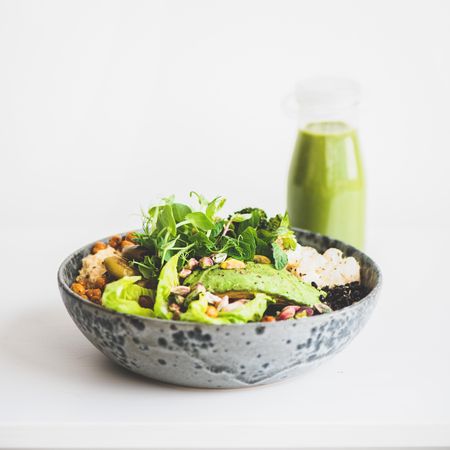 Healthy vegetarian bowl pictured of light background with smoothie on side, square crop