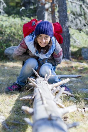 Female sitting on log in the forest in sweater and red backpack