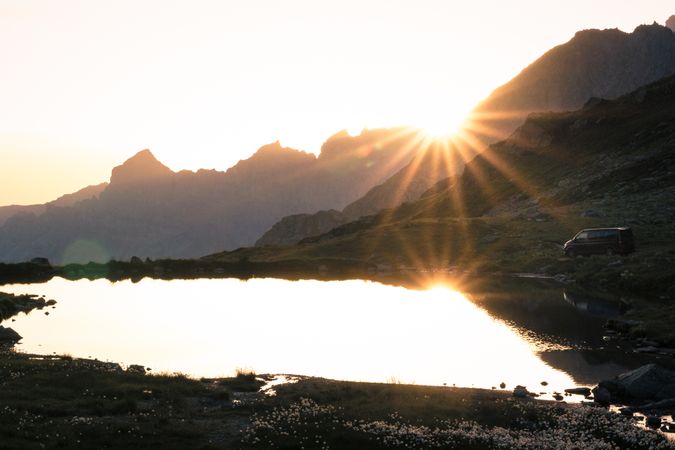 Car riding along shiny lake in sunlight in mountains