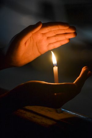 Hands surrounding lit candle during nighttime
