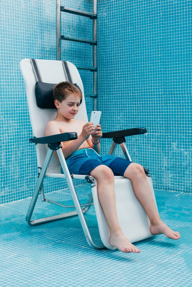 Boy with smartphone sitting on bottom of empty pool