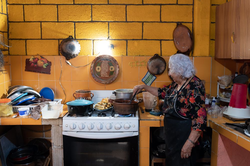 A woman is preparing red chili sauce to go with battered poblano chiles using a gas stove