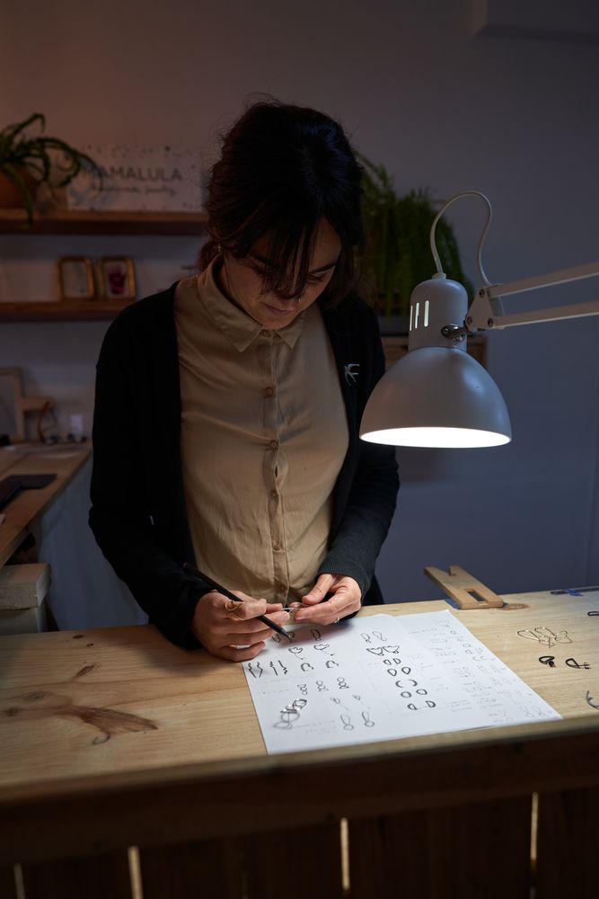Focused female jeweler with ring and sketches at table