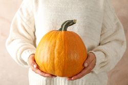 Young woman holding pumpkin on brown background, close up