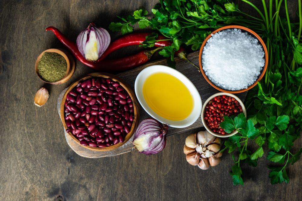 Top view of bowls of kidney beans, oil, pepper, garlic bulb, cilantro and onions