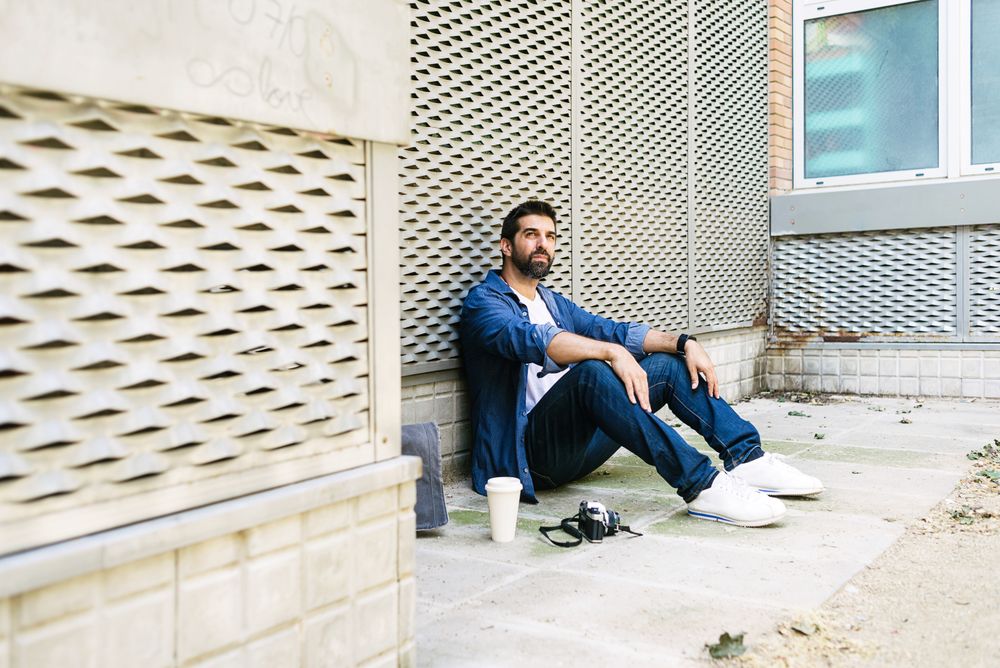 Latino man in denim sitting outside with cup of coffee
