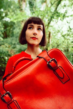 Woman in red with big red suitcase in forest