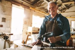 Happy mature male carpenter at his workshop holding power drill bGxVv0