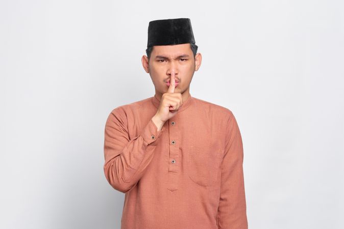 Muslim man in kufi cap making “shhh” gesture with hand over mouth