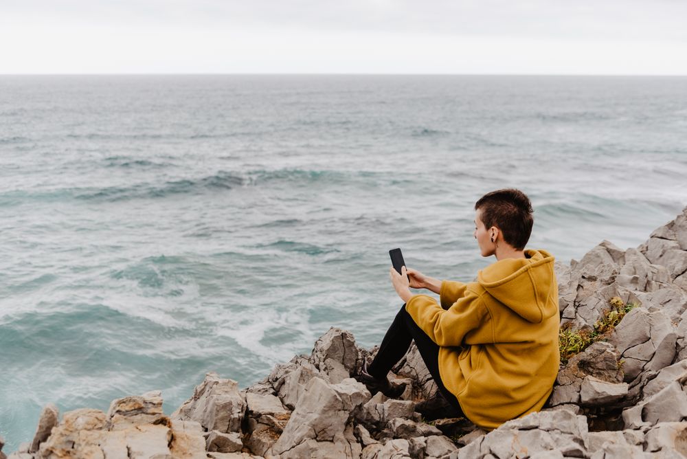 Woman in yellow hoodie taking selfie on smartphone on rocky shore