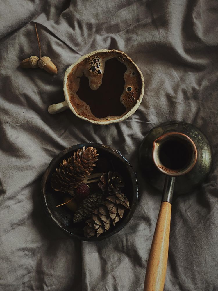 Top view of cup of Turkish coffee surrounded by pine cones on grey bedding