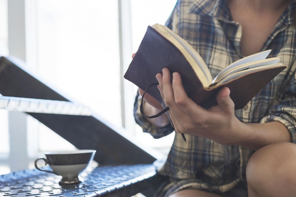 Unidentified woman reading from notebook on staircase with tea cup