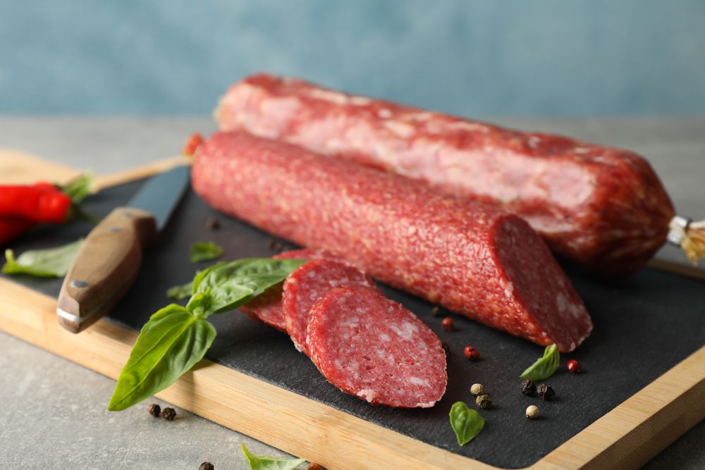 Side view of two sticks of cured meats with slices on wooden board