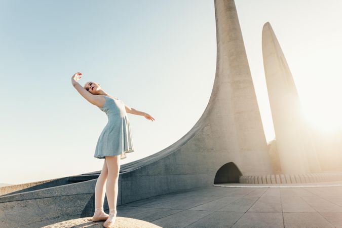 Slender woman posing in ballet position while standing on structure outdoors