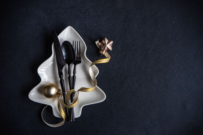 Dark cutlery on dark background tied with festive gold ribbon on tree shaped plate