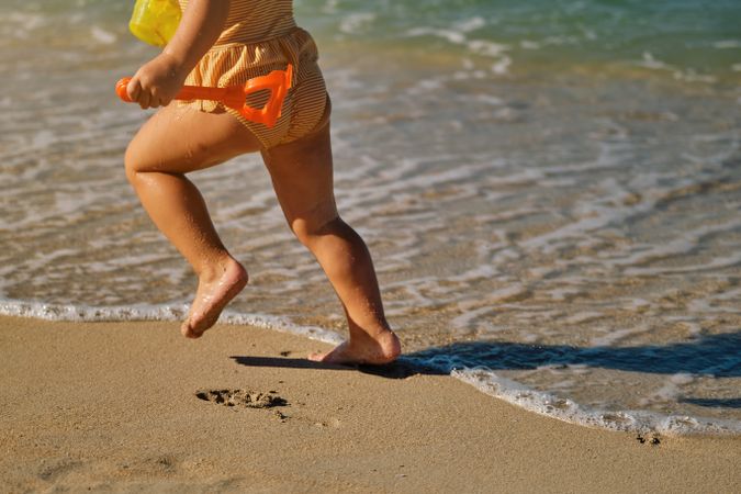 Crop girl running on sandy beach next to sea