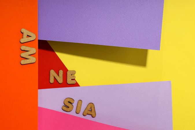 Scattered cork letters spelling “amnesia” on multi-colored paper background