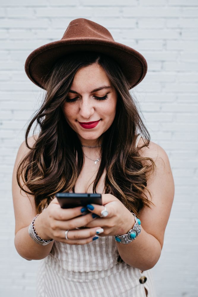 Woman in hat smiling browsing smartphone