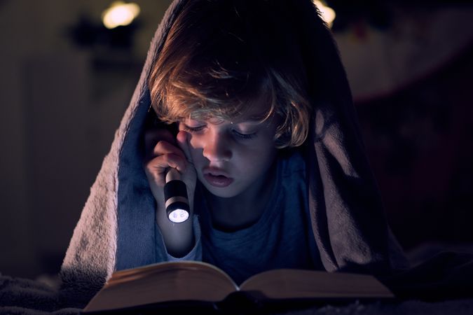 Serious boy reading book in dark apartment