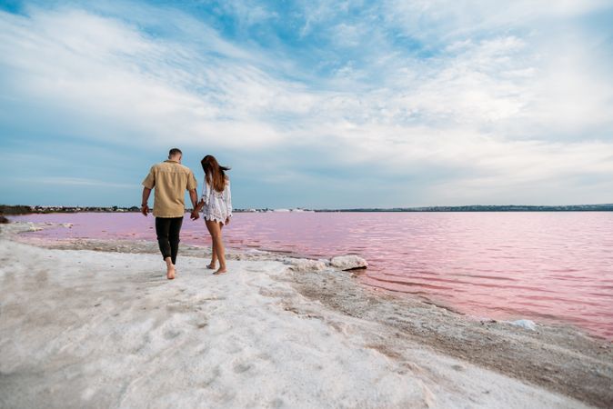 back view of adorable couple walking on an amazing beach with pink water