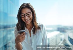 Woman wearing eyeglasses smiling while looking at her mobile phone 5aWYKb
