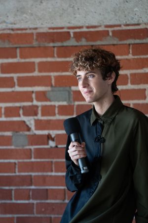 Nonbinary person holding microphone in front of brick wall