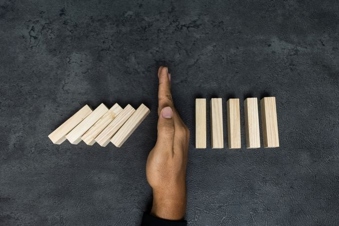 male hand stop falling wooden blocks. domino effect or risk protection strategy concept